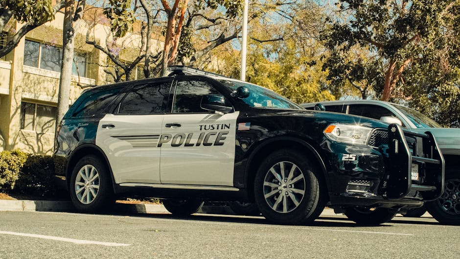 Tustin police car parked in a shaded lot surrounded by trees.