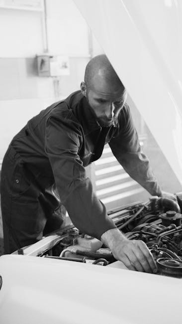 Male mechanic working under a car hood in a workshop, focusing on engine repair.