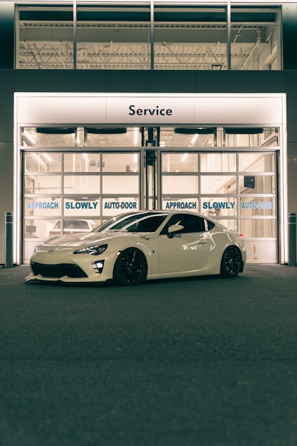A modern white sports car parked in front of an auto service garage at night.
