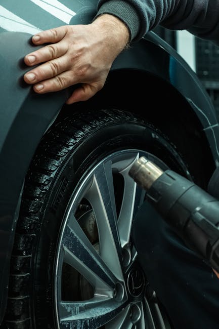 Hands working on a car tire using a heat gun, showing automotive maintenance in a workshop setting.